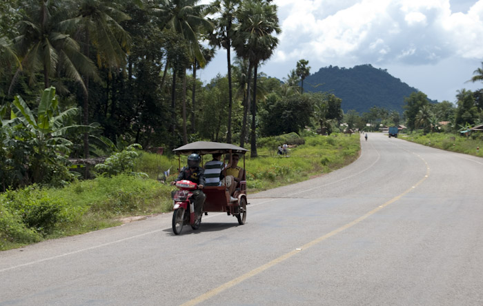 tuk-tuk on curved road with hill in background